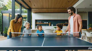 A modern, well-lit home with a family spanning three generations gathered around a ping pong table, smiling and engaged in play